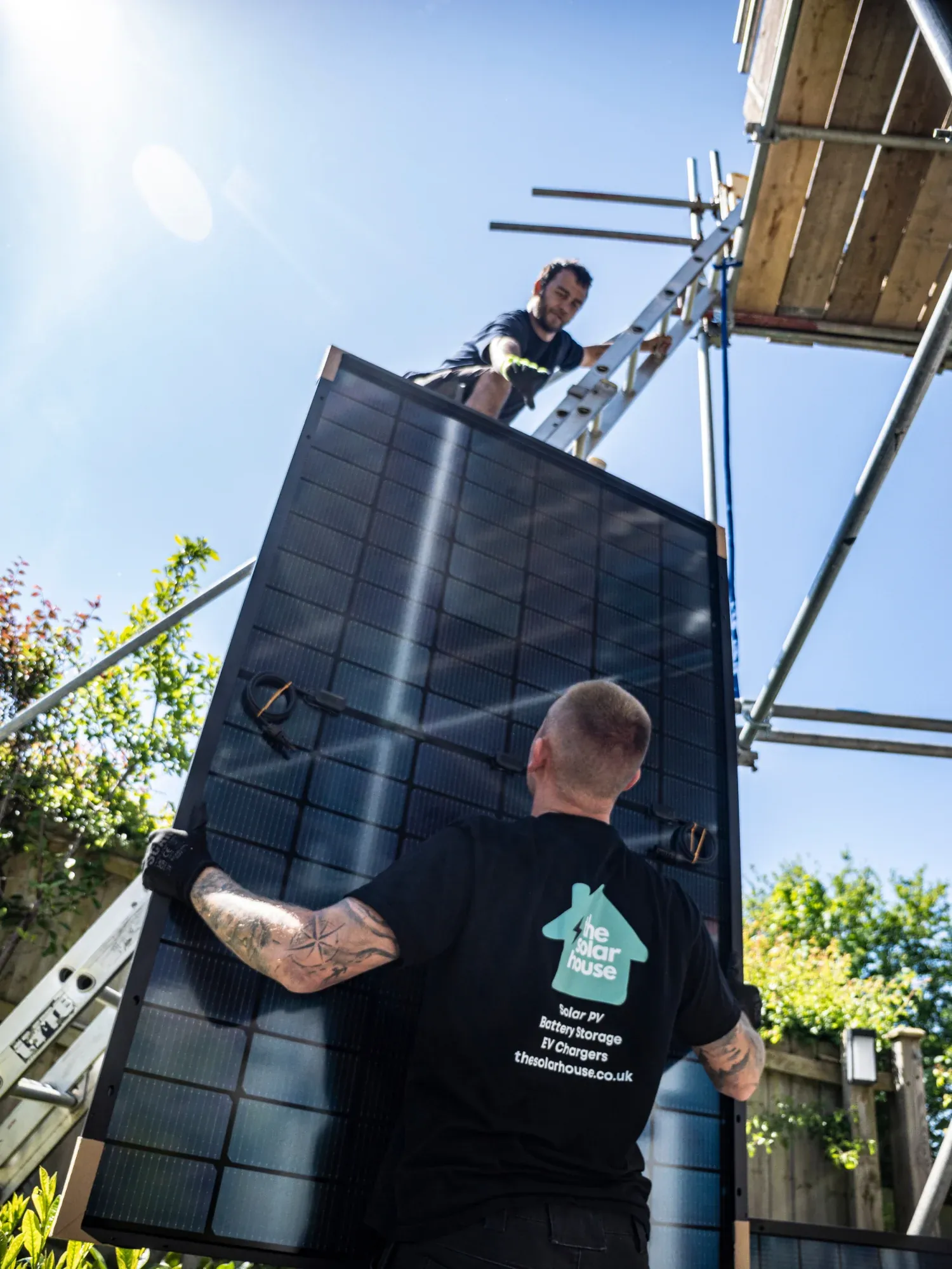 Two Solar House installers passing a solar panel up the scaffold to the roof