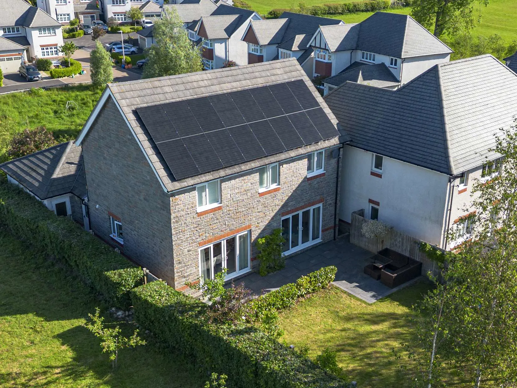 Drone view of a stone-fronted home with a full row of black solar panels on the roof