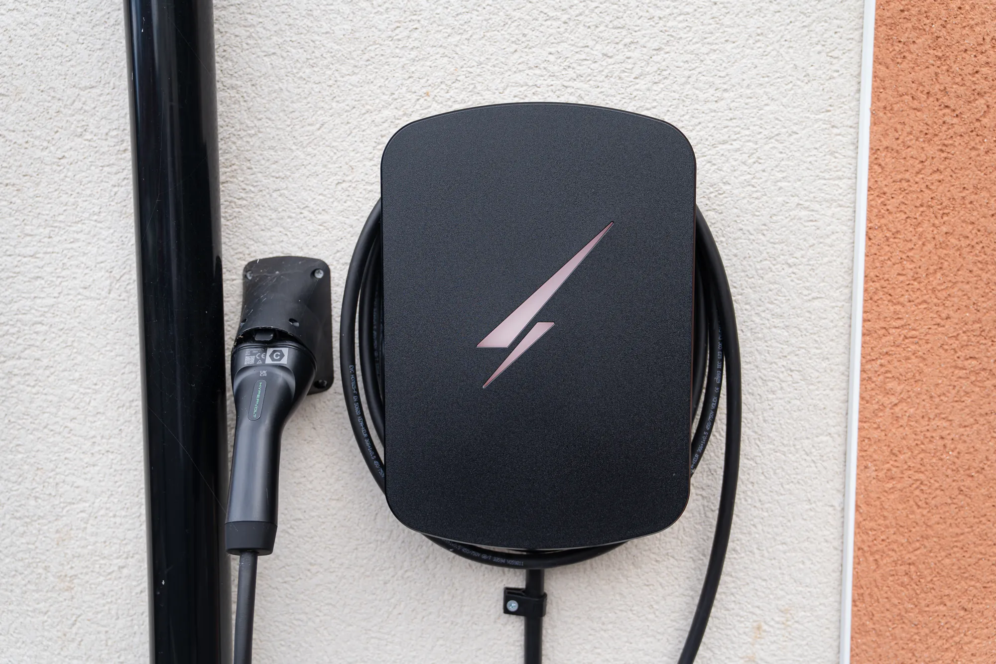 A black Hypervolt EV charger fitted to a white rendered wall, its cable coiled neatly behind