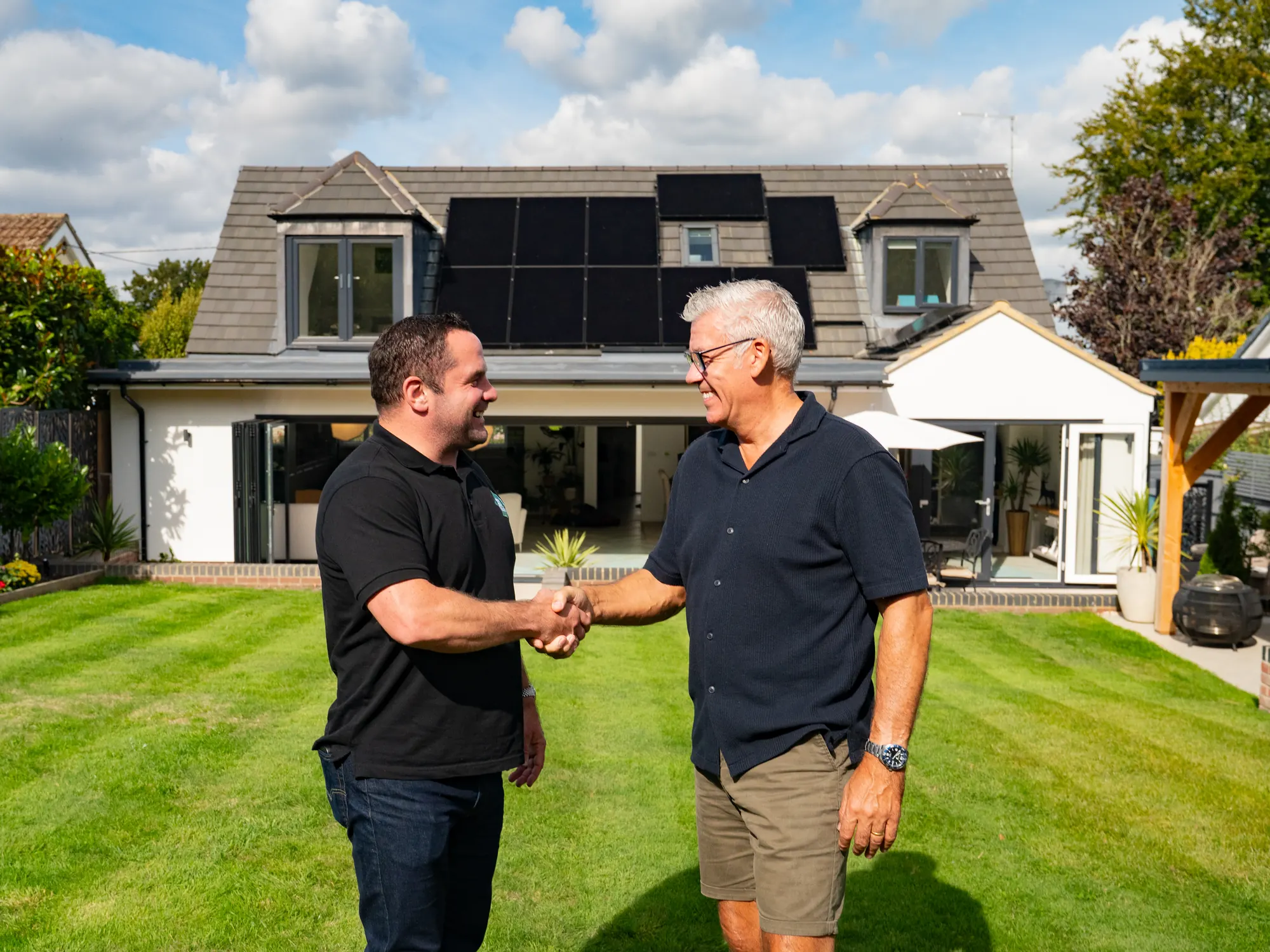 A Solar House adviser shaking hands with a homeowner on the lawn, solar panels on the house behind